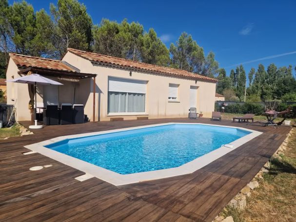 Maison avec piscine entourée d'un espace extérieur, dans un cadre ensoleillé.