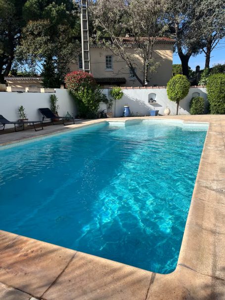 Piscine claire entourée de jardins et de chaises longues au soleil.