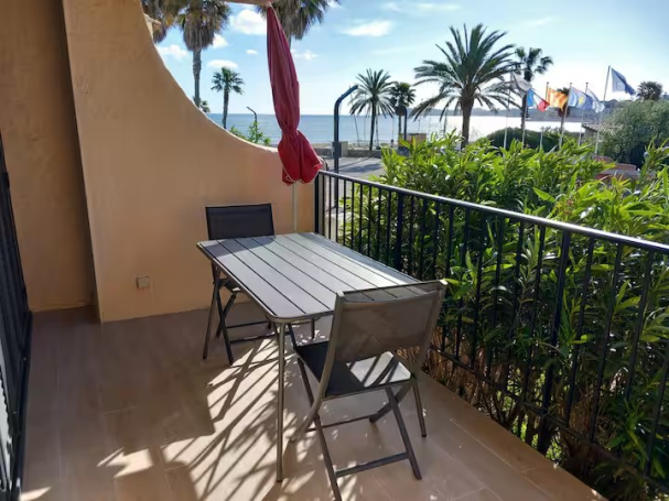 Marines de Cogolin: studio 2/4 pers, terrasse, pieds dans l'eau Balcon ensoleillé avec table et chaises, vue sur la mer et les palmiers.