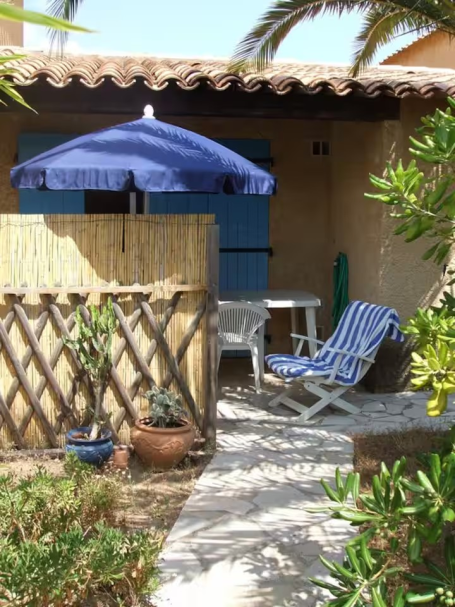 Cavalaire: maisonnette T3, piscine, jardin Terrasse d'une maison avec parasol bleu, chaises blanches et verdure environnante.