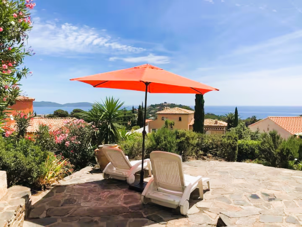 Cavalaire: maison T4, vue mer, jardin, calme Chaises longues sous un parasol orange, vue sur la mer et des maisons alentour.