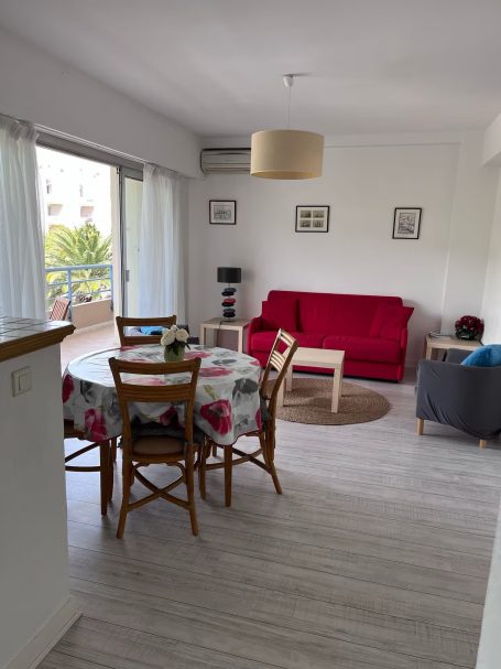 Le Méditerranée : proche mer, plein centre, garage Salon lumineux avec canapé rouge, table à fleurs et accès à un balcon.