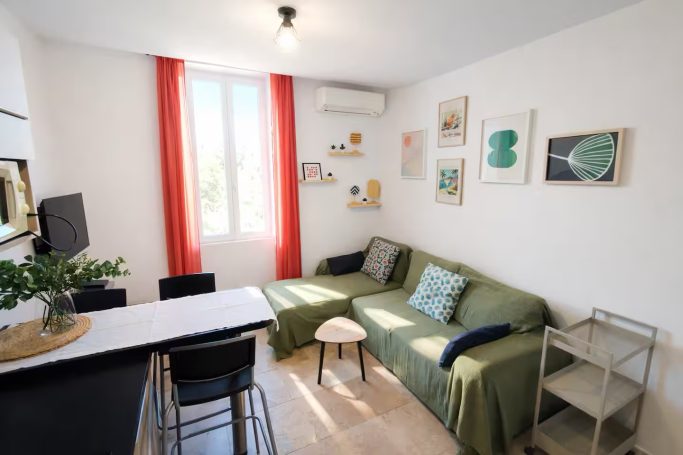 L'Escale en Provence, cœur de village & climatisé Salon lumineux avec un canapé vert, table, chaises et décorations murales.